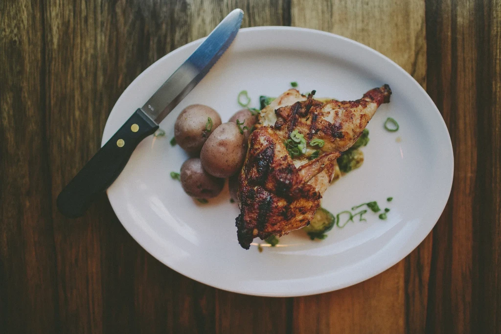 Grilled chicken with potatoes and green vegetables on a white plate.