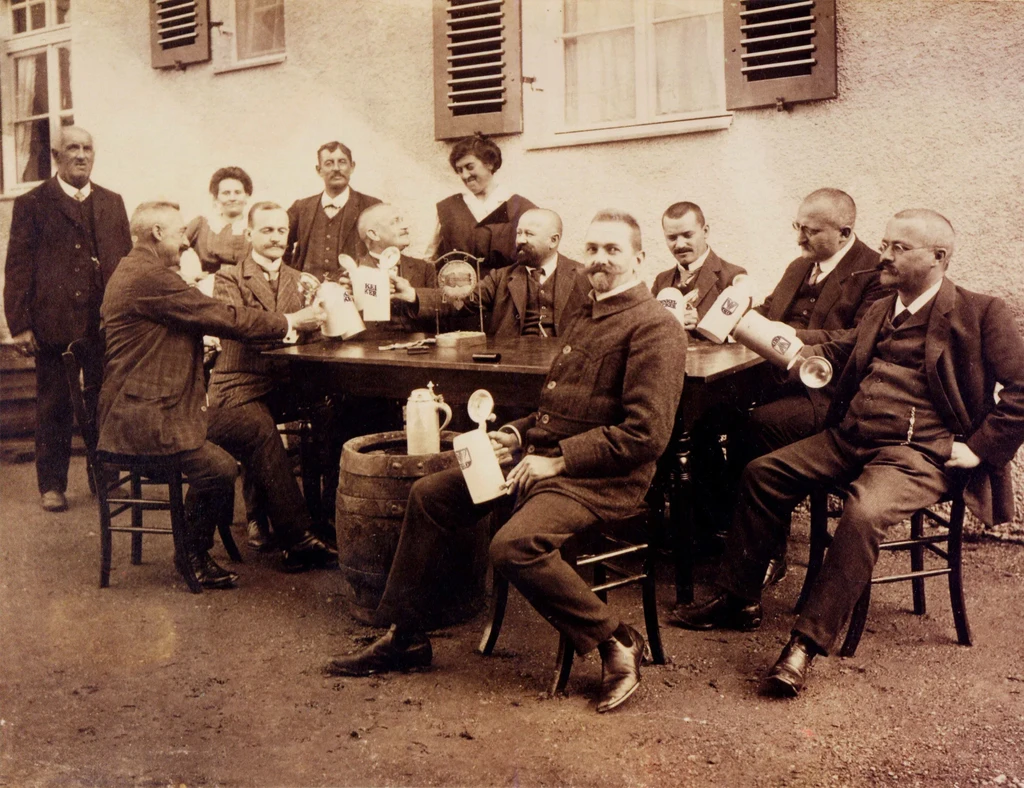 Vintage sepia photo of men toasting with steins outdoors.
