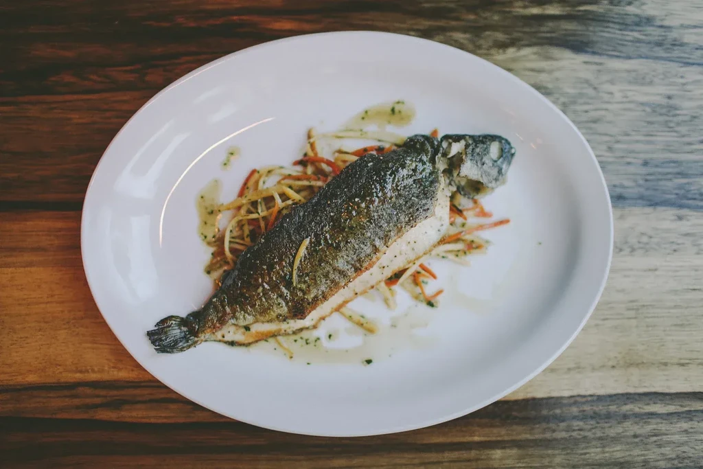 Golden-brown whole fish on julienned vegetables with green sauce.