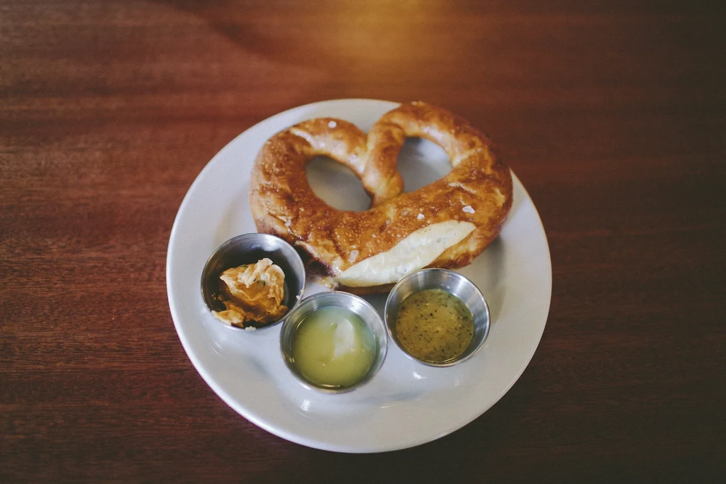 Salted soft pretzel with three unique dipping sauces on a plate.