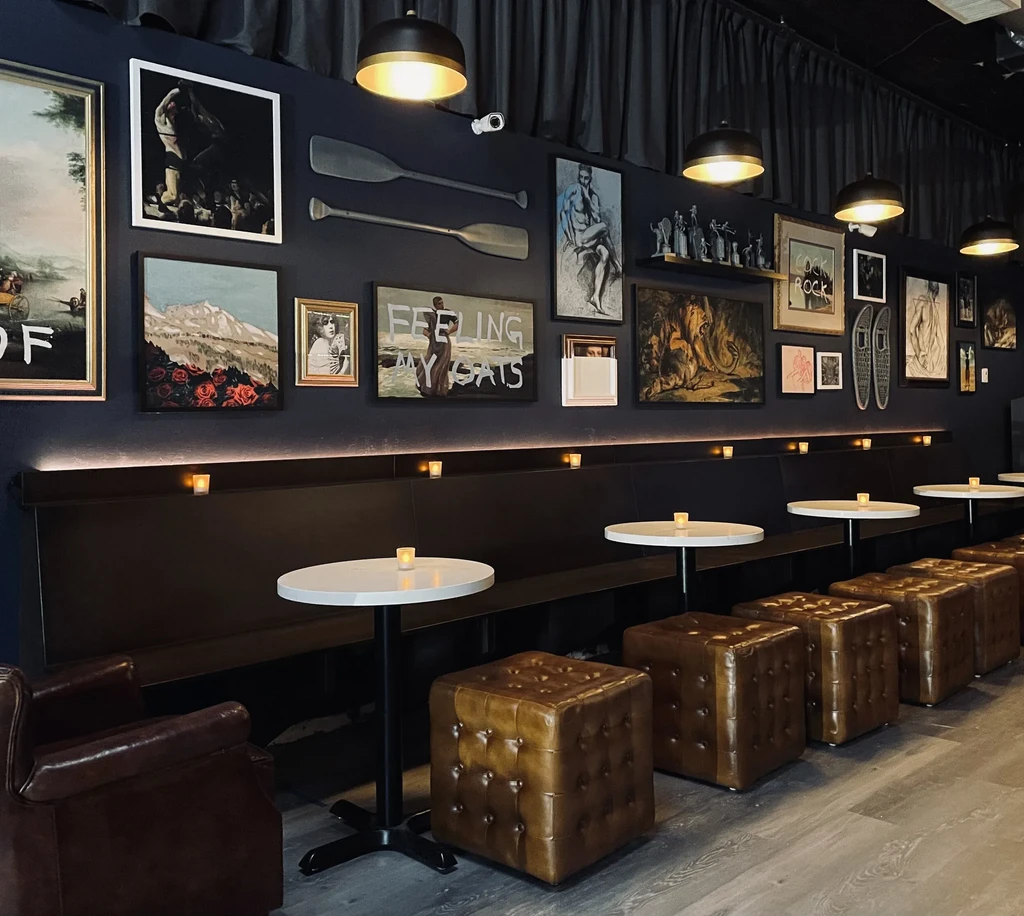 Dark restaurant interior with banquette seating, tables, and eclectic gallery wall.