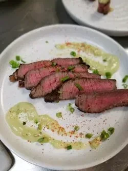 Fanned medium-rare steak with green sauce, green onions, and red spice.