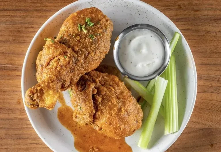 Overhead view: Fried chicken, orange-red sauce, celery, and creamy dip.