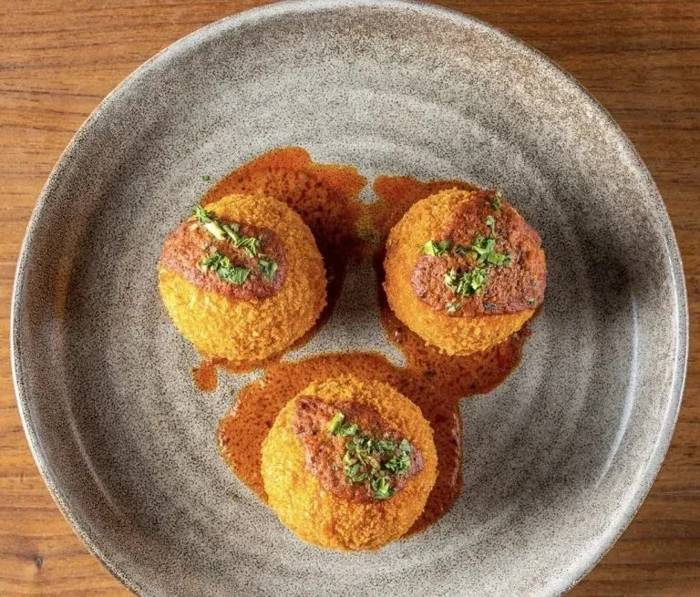 Three arancini with tomato sauce and herbs on a gray plate.