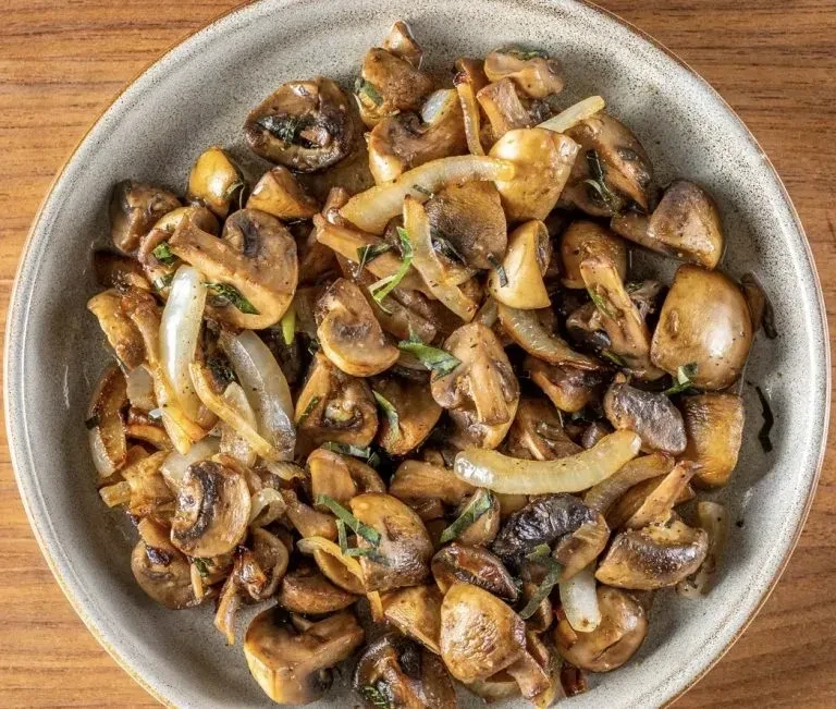 Close-up of sautéed mushrooms and onions with herbs in a ceramic bowl.
