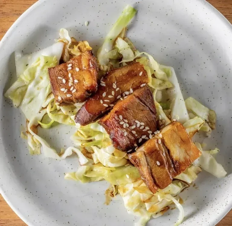 Golden pork belly with sesame seeds and cabbage on a gray plate.