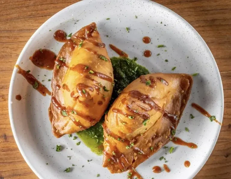 Two golden flaky pastries with brown glaze, herbs, and green sauce.