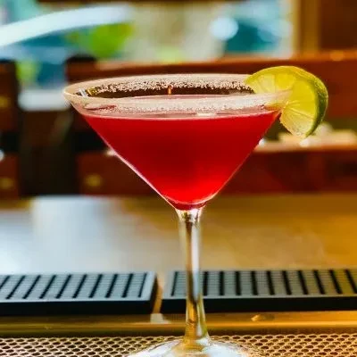 Red cocktail in martini glass with sugared rim and lime wedge.