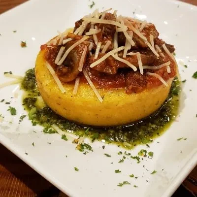 Plated polenta topped with mushroom ragu, Parmesan, and herb oil.