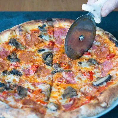 Hand slicing a freshly baked pizza with pepperoni, mushrooms, and cheese.