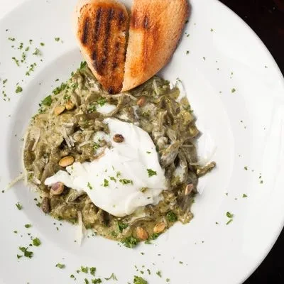 Green food with creamy topping, pine nuts, and grilled bread slices.