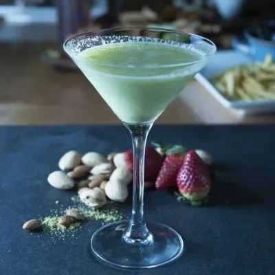 Green creamy drink in martini glass with frothy rim, nuts, and strawberries.
