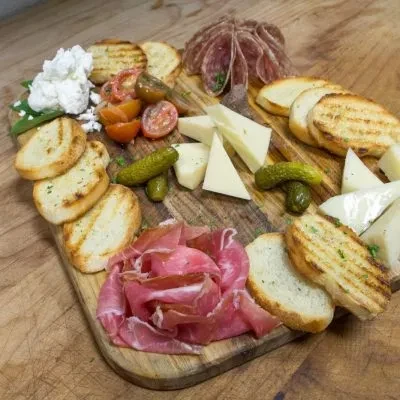 Charcuterie board with grilled bread, cheeses, cured meats, tomatoes, pickles.