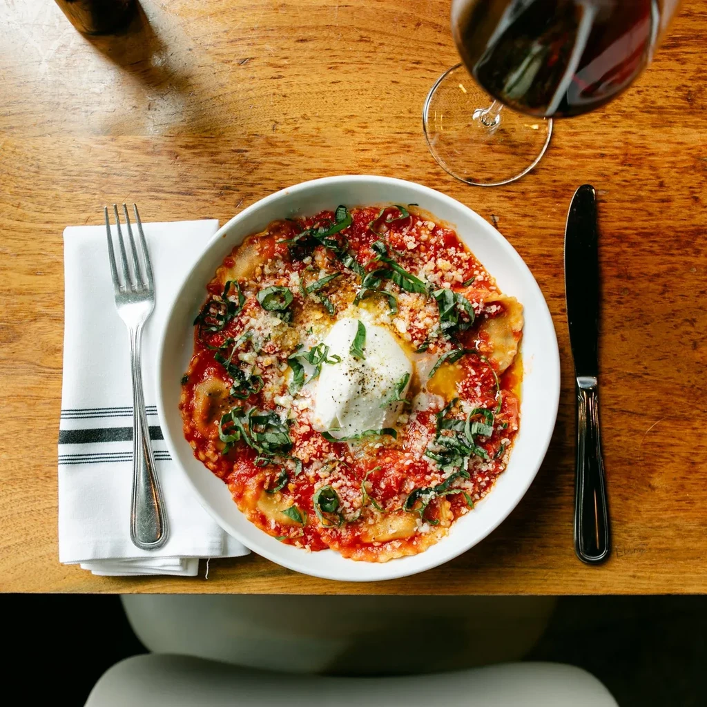 Top-down view of pasta with tomato sauce, basil, cheeses, and wine.