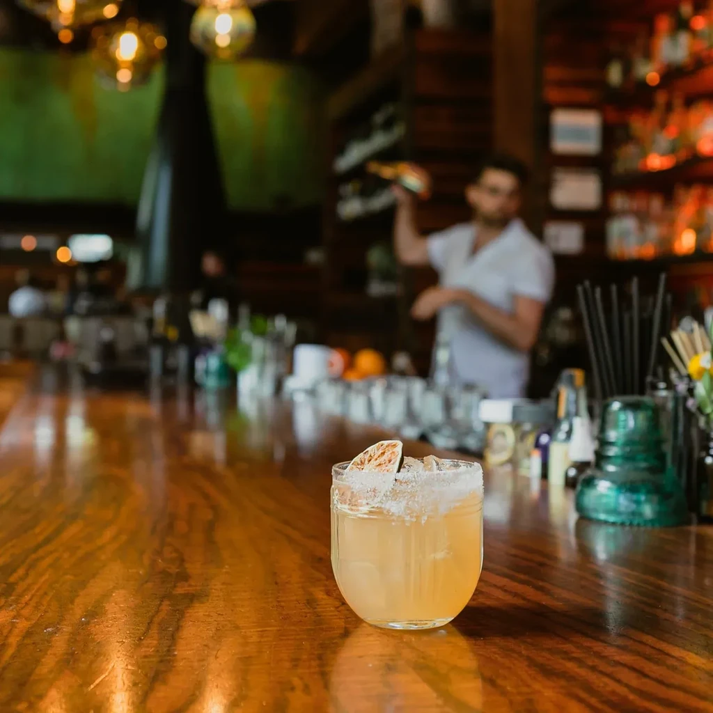 Amber cocktail with salt rim and citrus on a wooden bar.