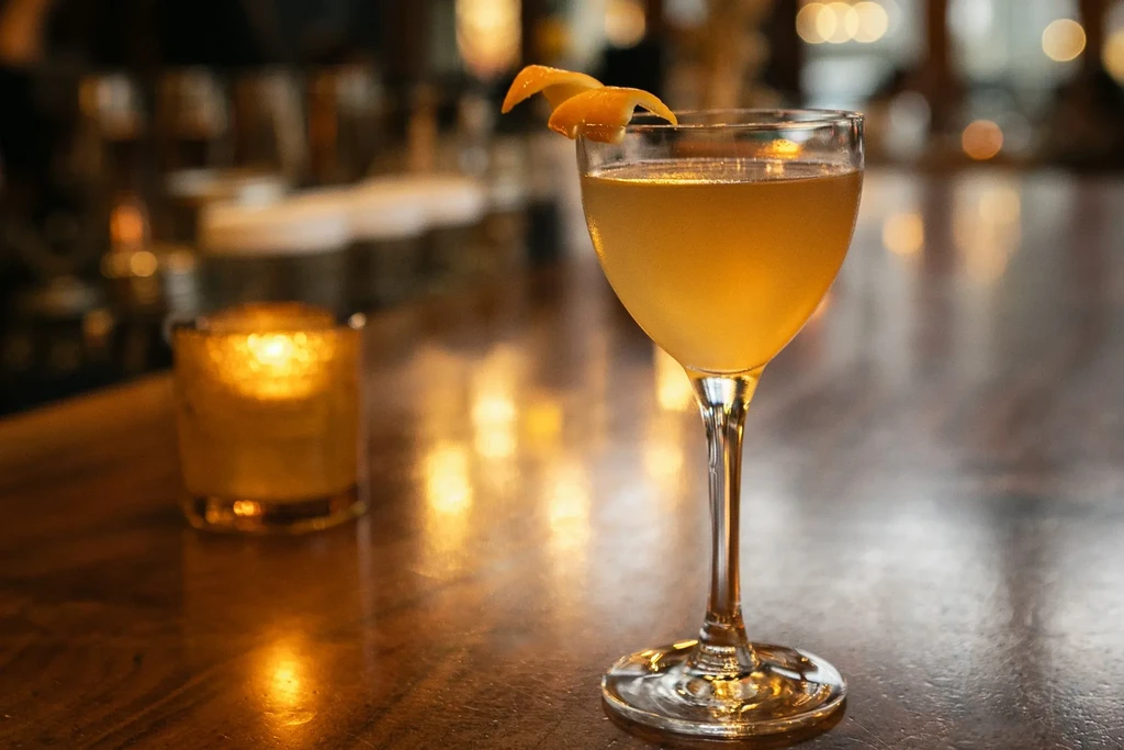Golden cocktail with orange peel, on a bar with candle glow.