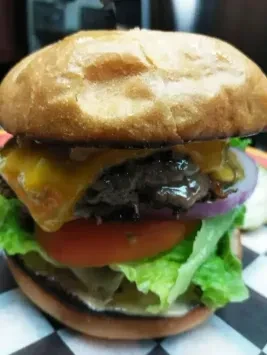 Burger close-up with melted cheese, patty, vegetables, on checkered paper.