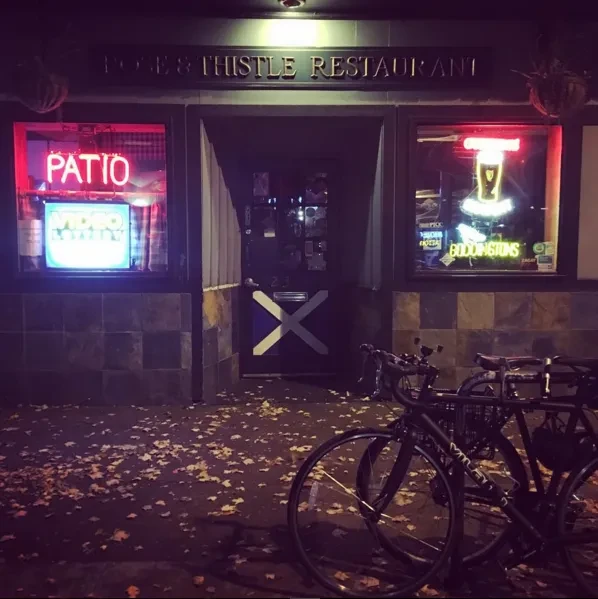 Night view of Rose & Thistle Restaurant with neon signs, parked bicycles.