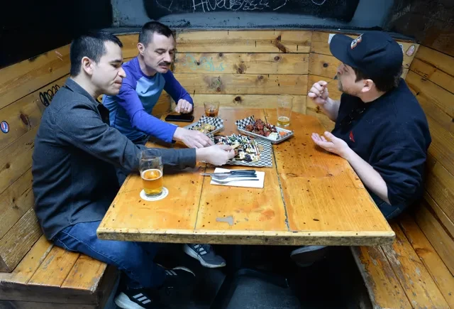 Three men share food and beer at a rustic restaurant booth.