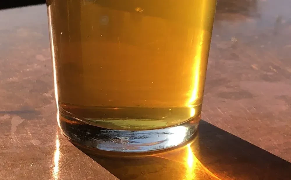 Golden beverage in glass on reddish-brown sunlit table.