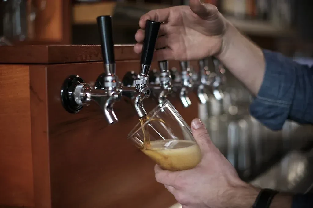 Hands pour frothy amber beer from a tap into a tilted glass.