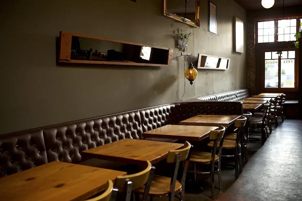 Empty restaurant interior with long dark leather booth and wooden tables.