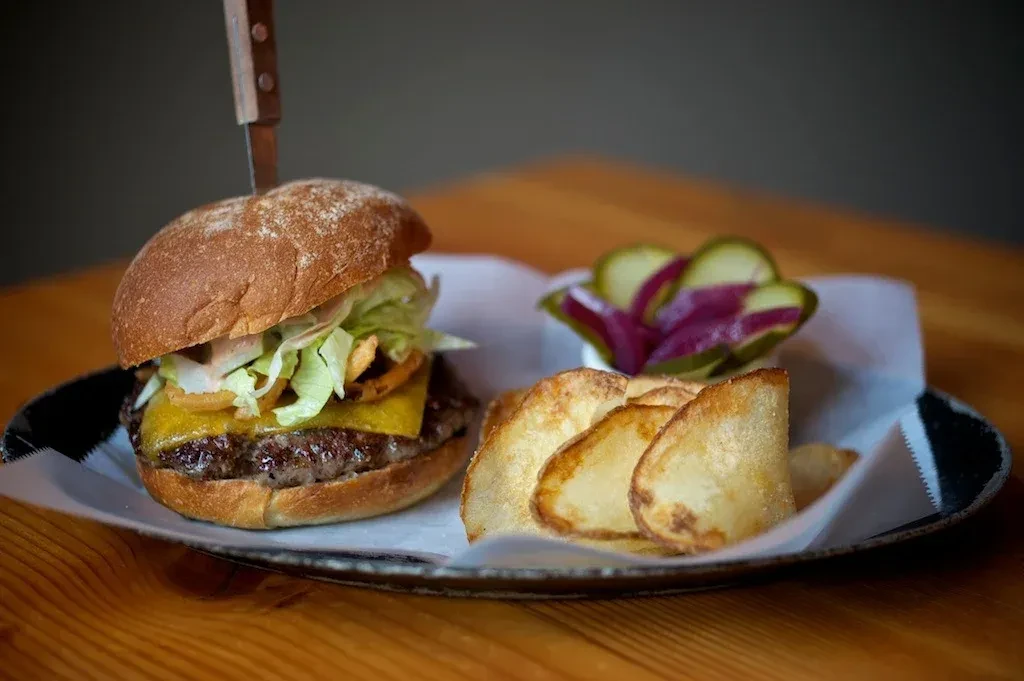 Close-up of burger with steak knife, potato wedges, and pickles.