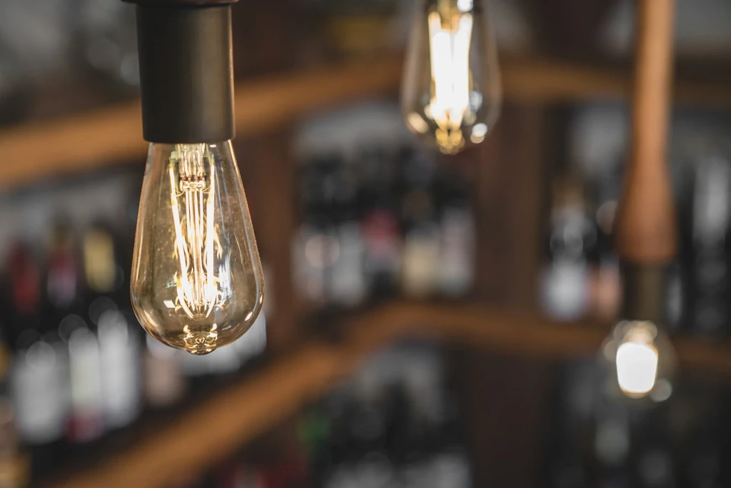 Illuminated teardrop Edison bulb, blurred wine bottles in background.