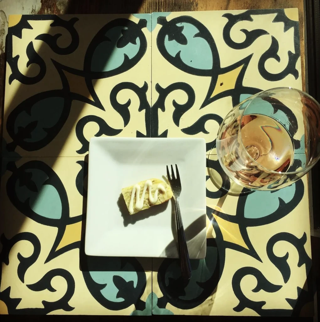Dessert, rosé wine, and fork on ornate patterned ceramic tiles.