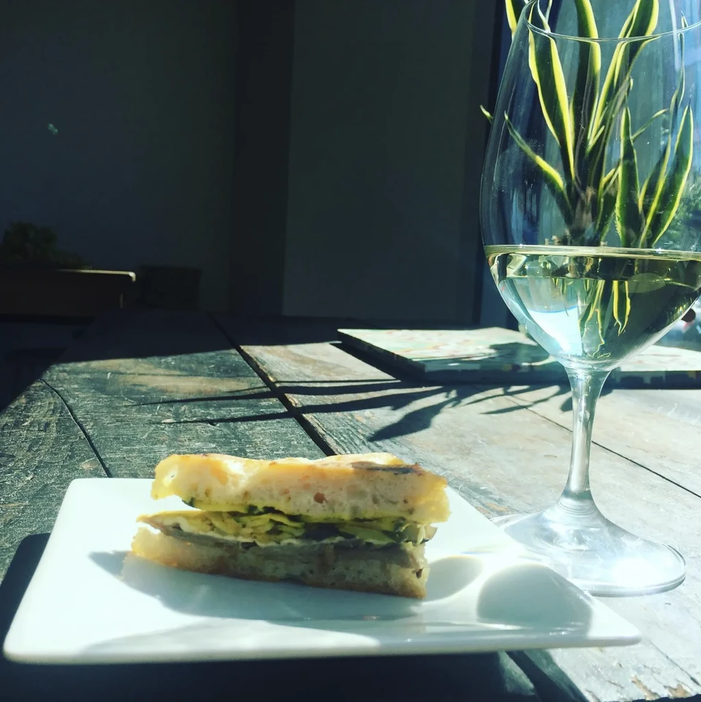 Rustic grilled sandwich and white wine on a sunny wooden table.