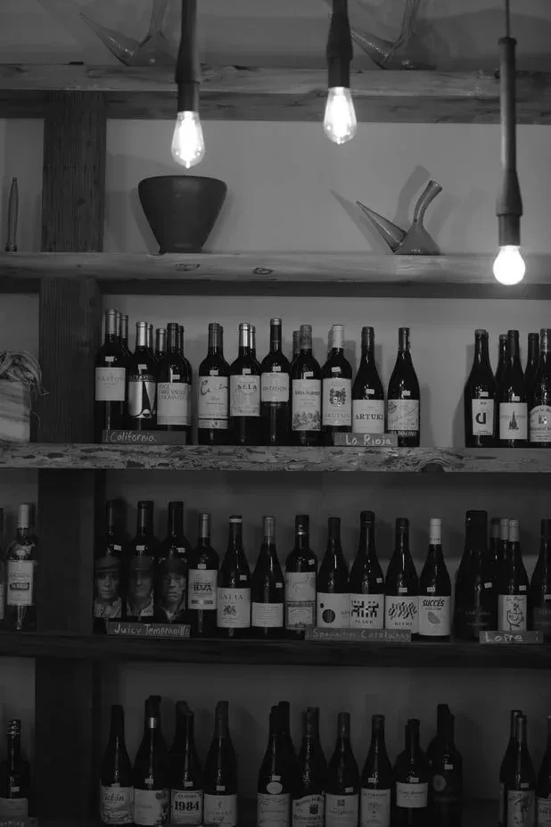 Black and white image: Wooden shelves packed with wine bottles, some with faces.