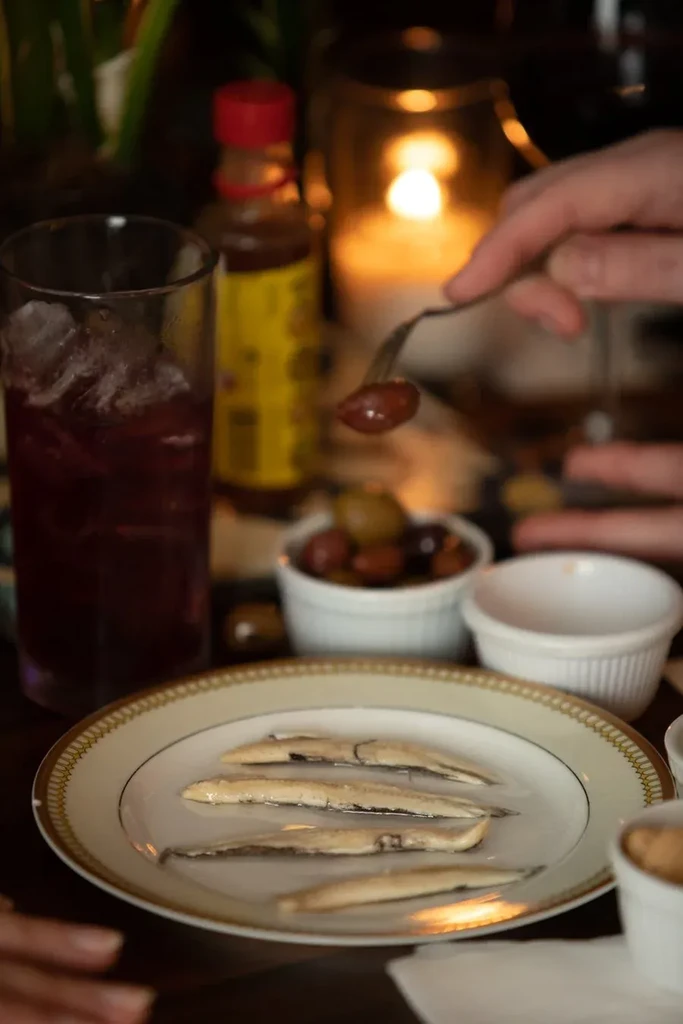 Close-up of dimly lit table with filleted fish, olives, and drink.