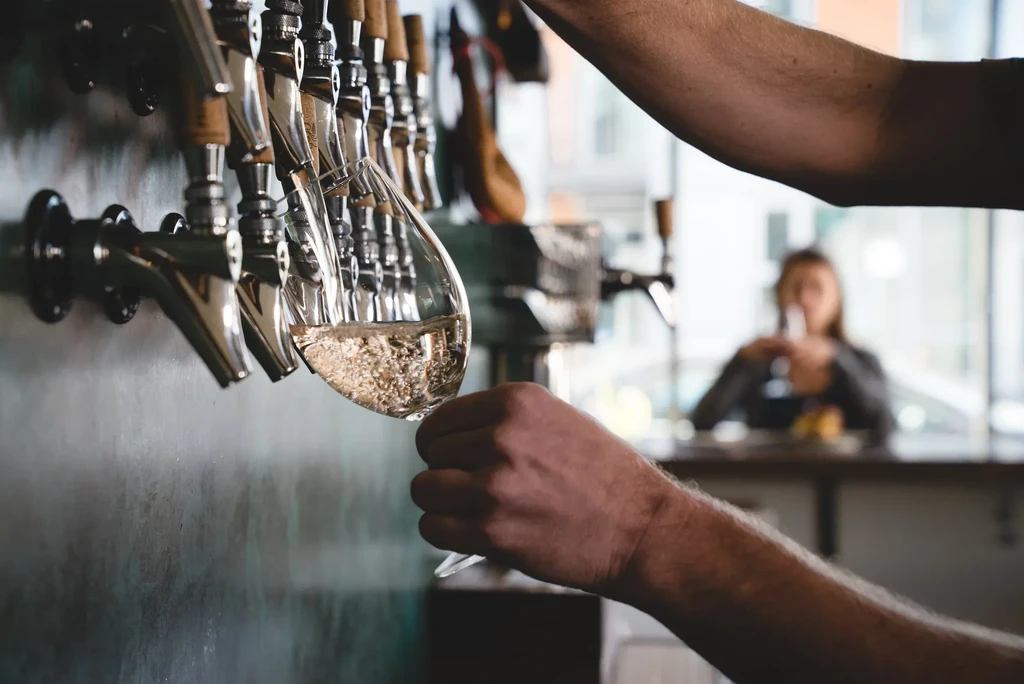 Hand fills wine glass with sparkling drink from chrome bar taps.