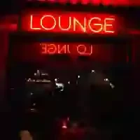 Bright red neon "LOUNGE" sign above a dark doorway, with reflection.