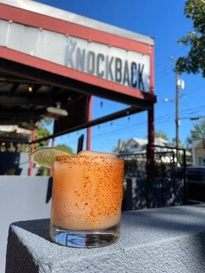 Frosty orange cocktail with spicy rim, lime, at 'THE KNOCKBACK'.