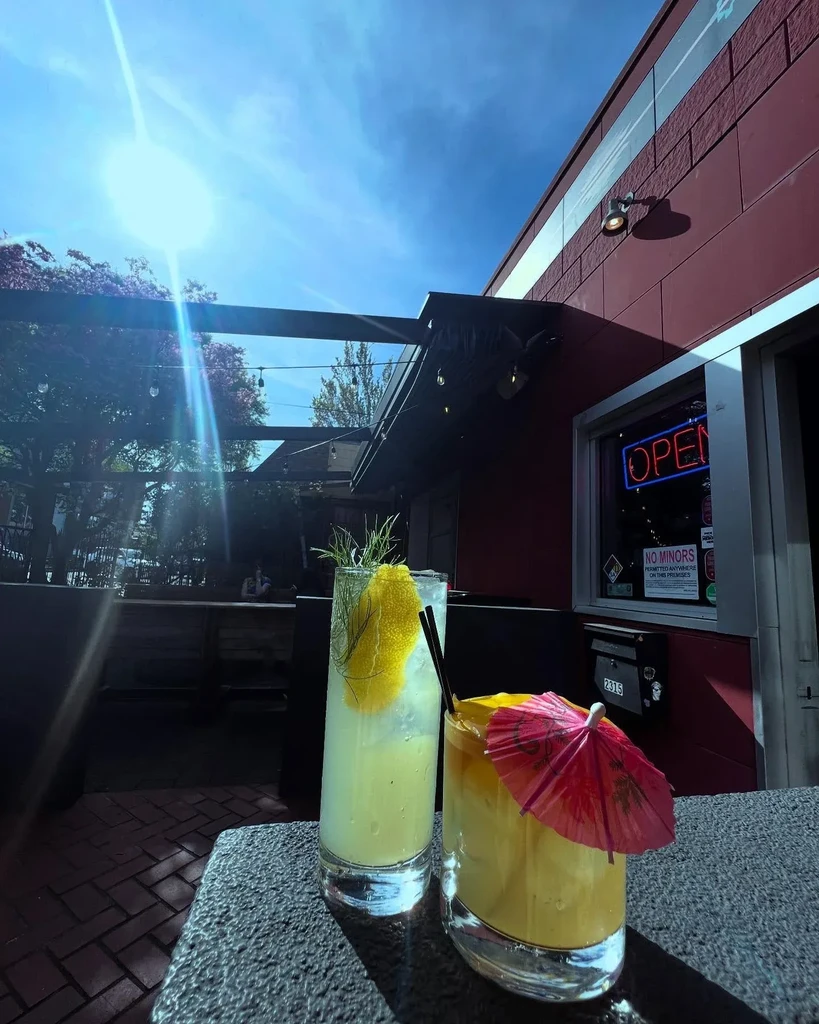 Two vibrant cocktails on a sunny outdoor patio near an 'OPEN' sign.