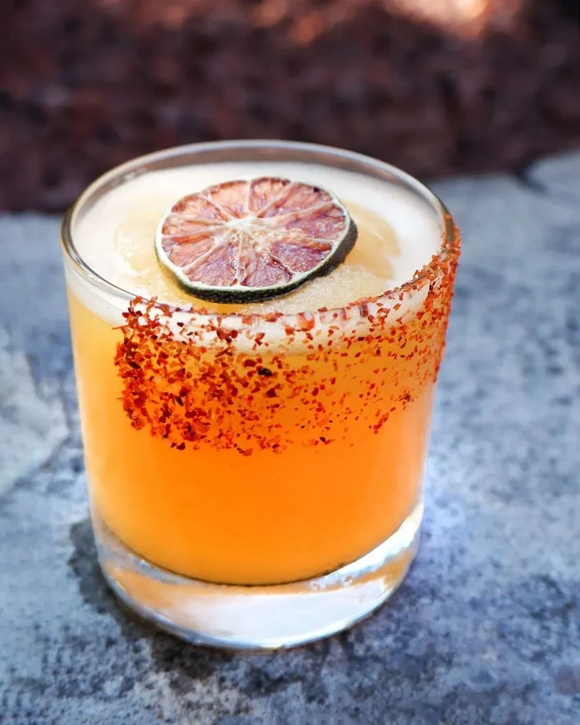 Close-up of an orange cocktail with spicy rim and dried citrus garnish.