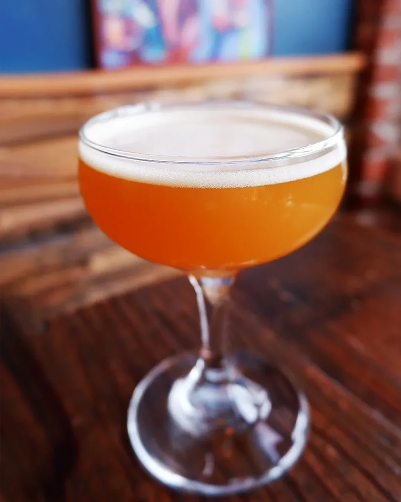 Orange drink with white foam in a coupe glass on wood.