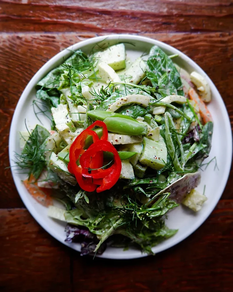 Fresh green salad on white plate with red pepper and snap pea garnish.