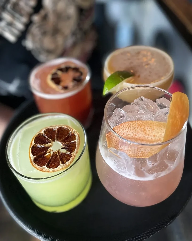 Close-up of four colorful cocktails with various garnishes on a black tray.