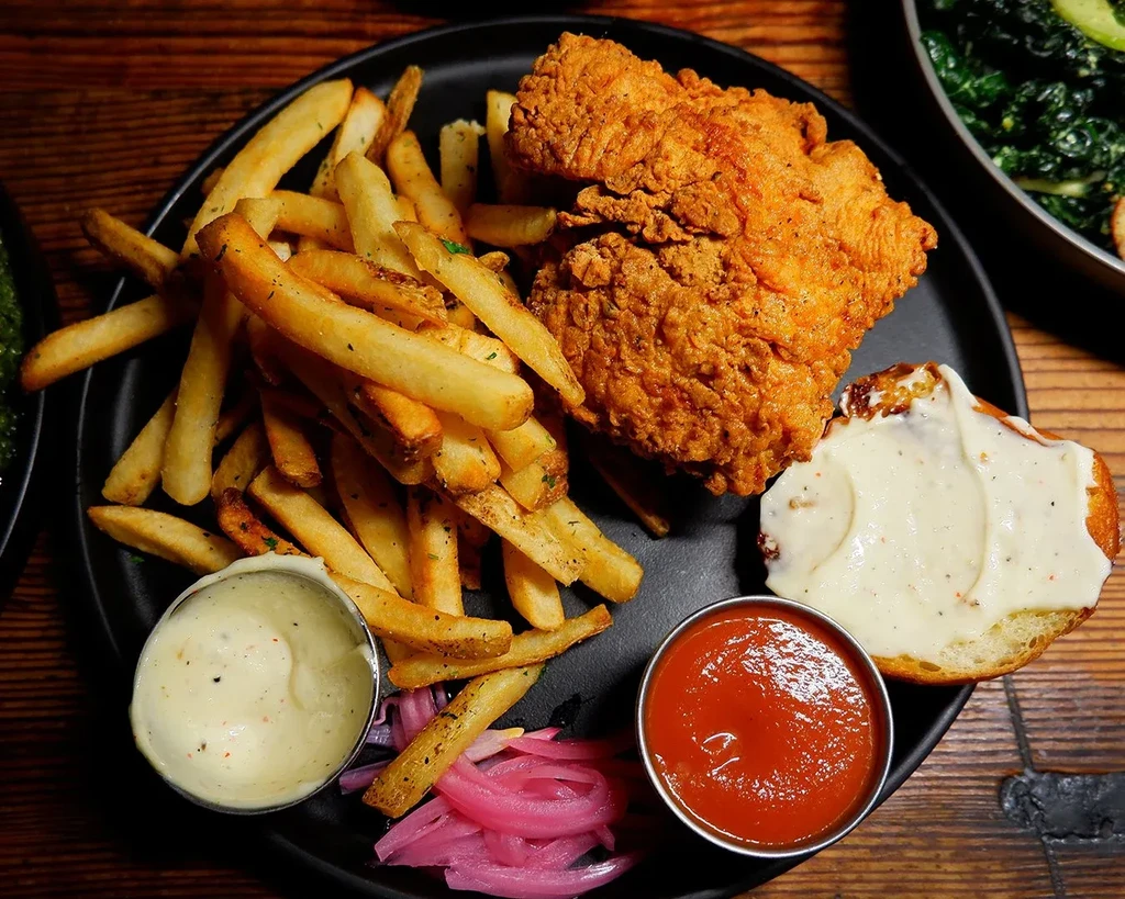 Crispy fried chicken, fries, pickled onions, sauces on a black plate.
