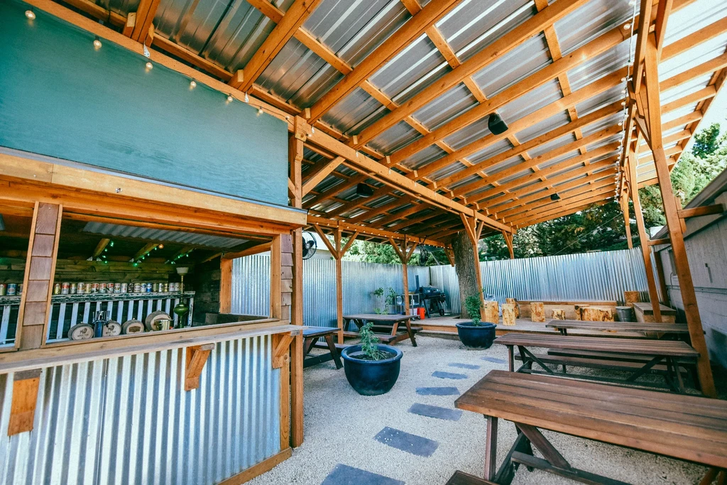 Rustic outdoor beer garden with wooden picnic tables, bar, and string lights.
