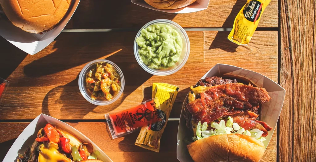 Overhead: sandwiches, guacamole, relish, and condiments on rustic table.