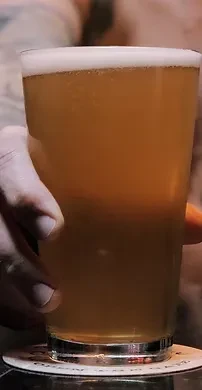 Close-up of hand holding foamy amber beer on a coaster.