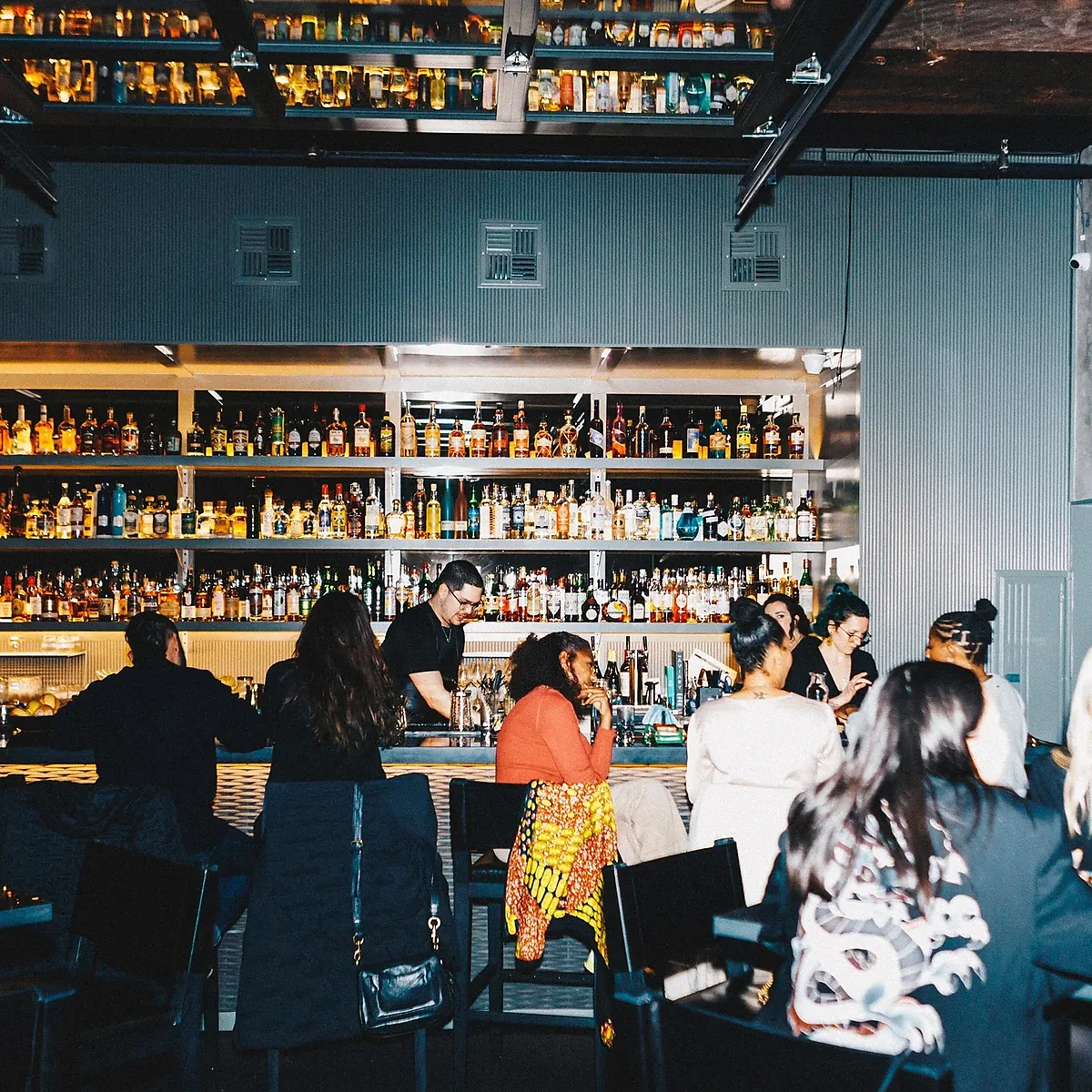 Busy bar room with guests seated along the lit back bar