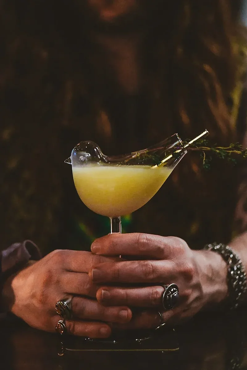 Yellow cocktail in bird-shaped glass held in both hands