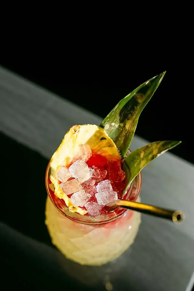 Red cocktail over crushed ice with pineapple leaf garnish