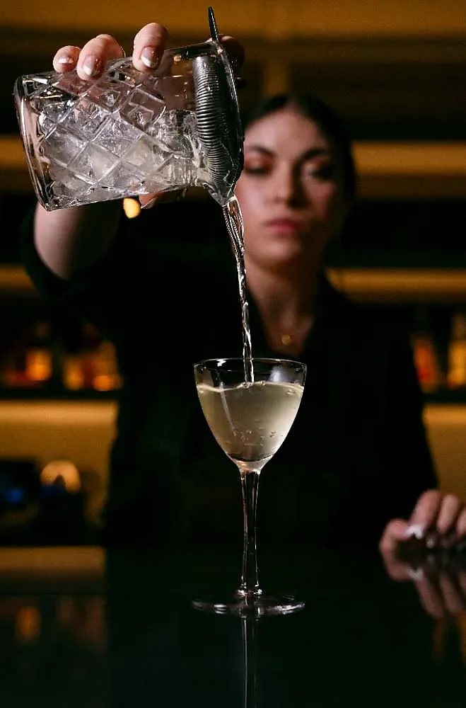Bartender straining a cocktail into a stemmed glass at bar