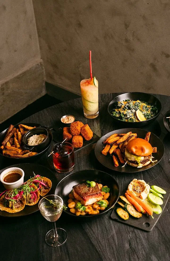 Table spread of shared plates, fries, tacos and cocktails