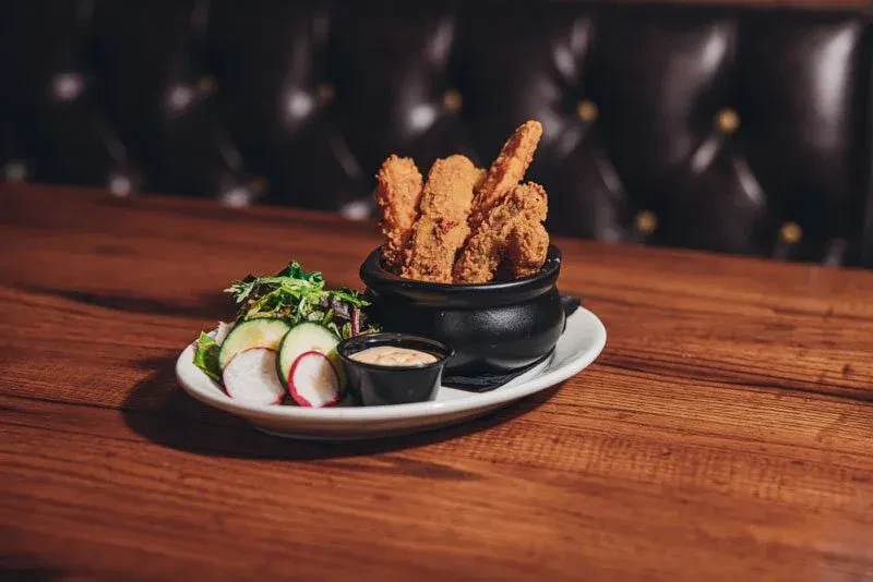 Crispy fried food, side salad, and dipping sauce on a rustic wooden table.